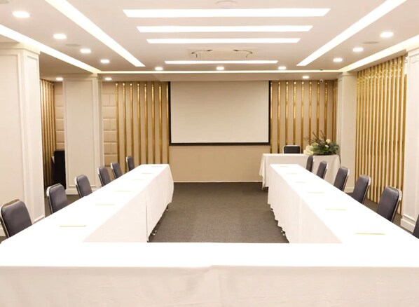 Un salón de conferencias con una larga mesa, sillas, una pantalla de proyector y un atril.
