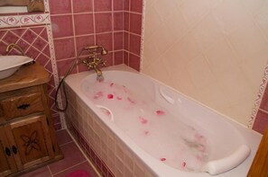 A bathroom with a bathtub filled with rose petals, a wooden cabinet with drawers, and pink tiled walls. - Casa Rural Aingeru (Valle de Carranza)
