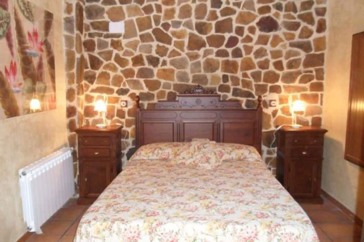 A bedroom with a stone wall, a floral bedspread, and two bedside tables with lamps.