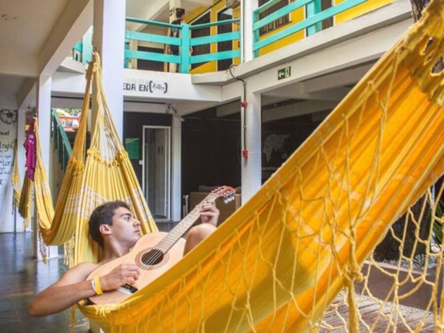 Une personne se détend dans un hamac à l'intérieur d'un bâtiment doté d'un balcon et d'une enseigne sur laquelle on peut lire « EDEN EN ».