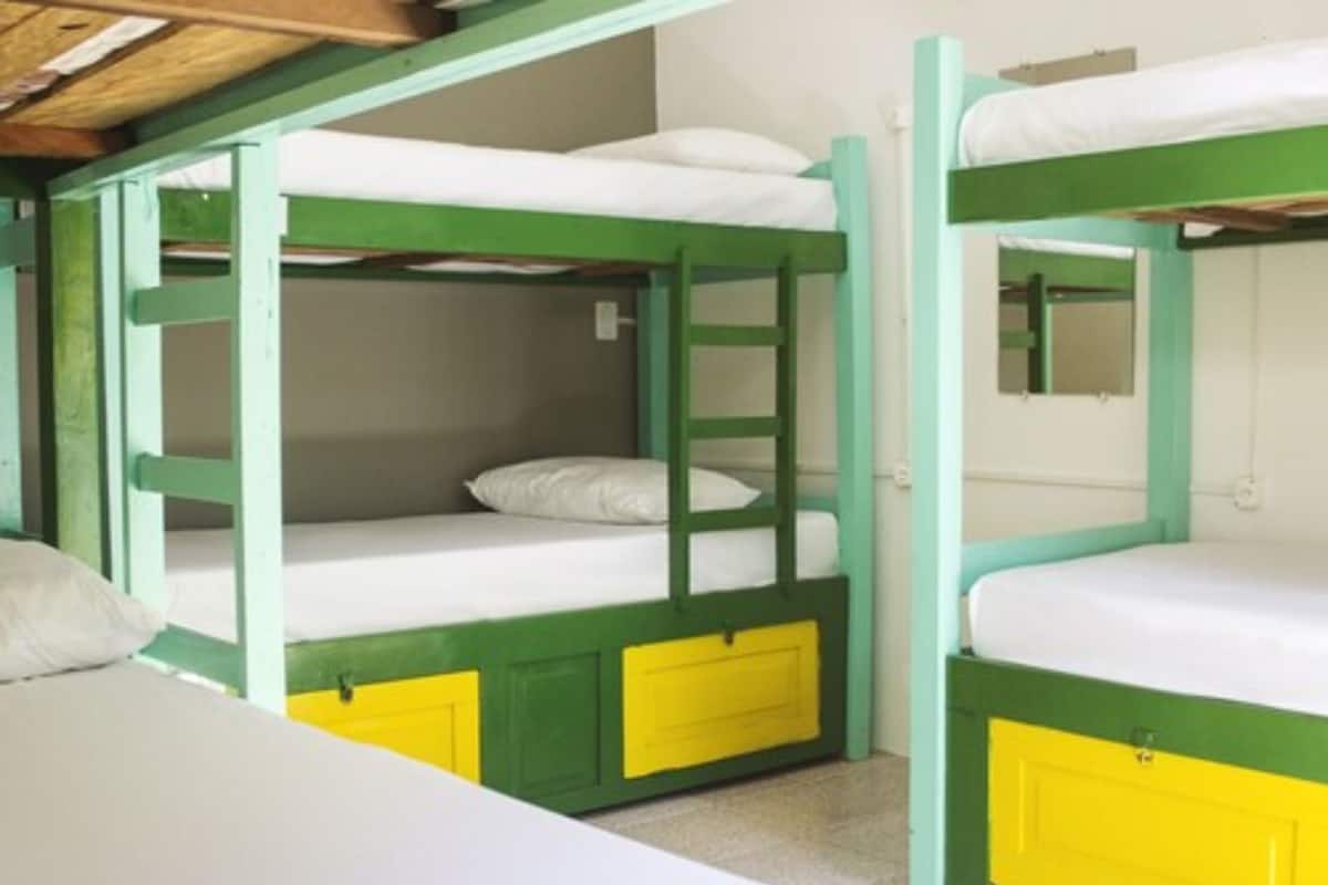 A bunk bed room with green and yellow accents, white bedding, and a small mirror on the lower bunk.