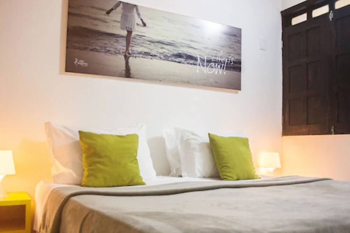 A bedroom with a bed, pillows, a nightstand, a wall-mounted painting, and a door.