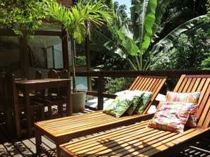 A wooden deck with a bench and chairs, surrounded by lush greenery and a large plant. - Che Lagarto Hostel Morro de São Paulo (Cairu)