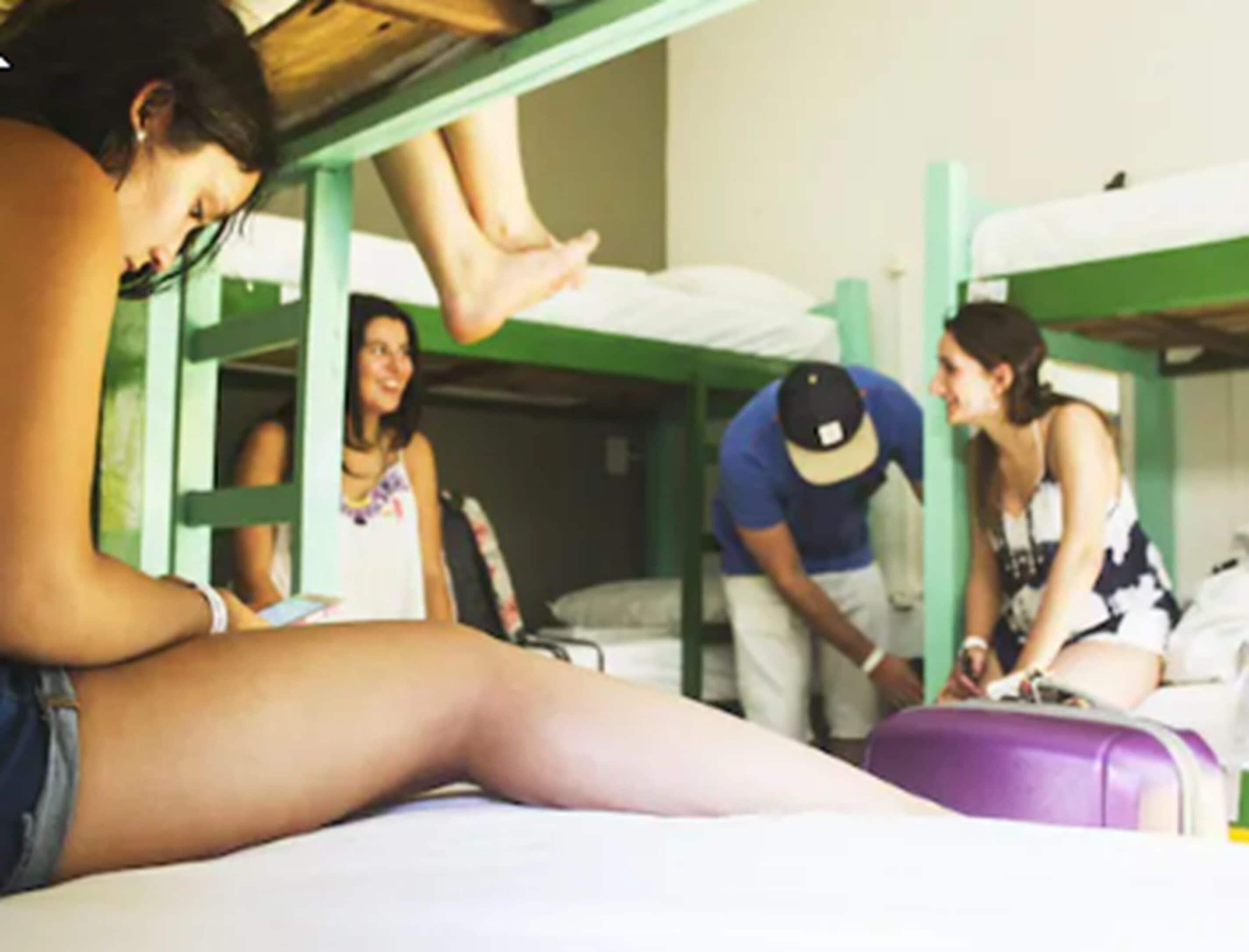 A dormitory room with bunk beds, a purple suitcase, and a person sitting on the floor.