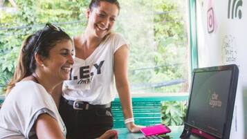 Two people at a desk with a computer, a pink phone, and a window with greenery outside.
