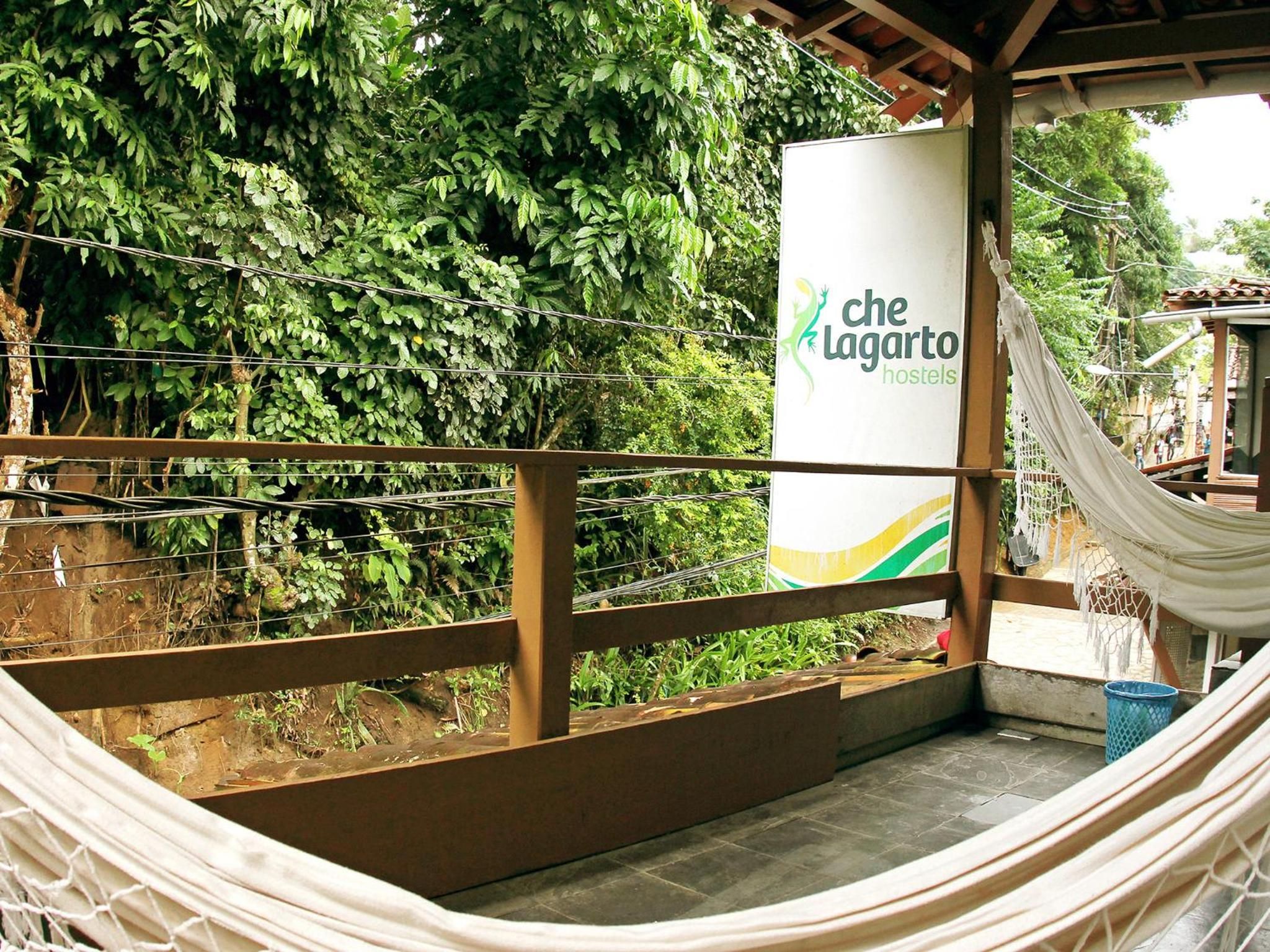 Una hamaca, un letrero de Che Lagarto Hostels y vistas de vegetación exuberante.