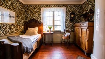 Un dormitorio con una cama de madera, una mesita de noche, una ventana con cortinas, un armario de madera y un reloj de pared.