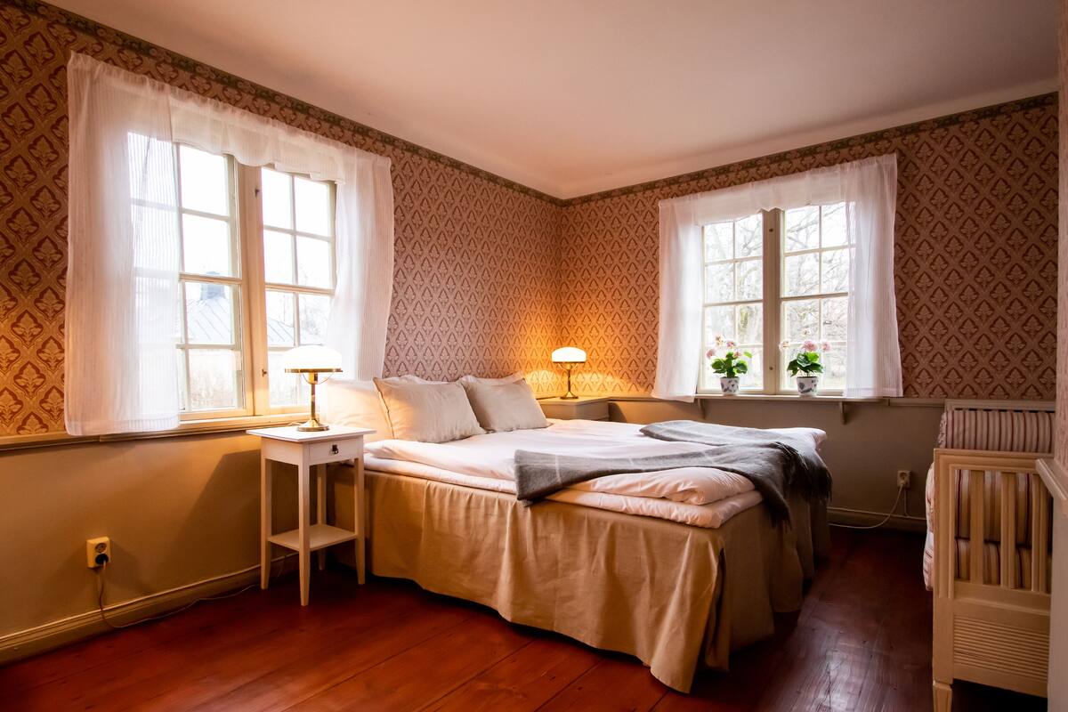 Un dormitorio con cama, mesitas de noche, lámpara y cuna.
