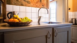 A kitchen with a sink, a fruit basket, and a kettle.