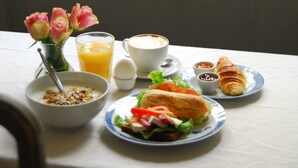 A breakfast table with a bowl of cereal, a glass of orange juice, a cup of coffee, a croissant, and a sandwich.