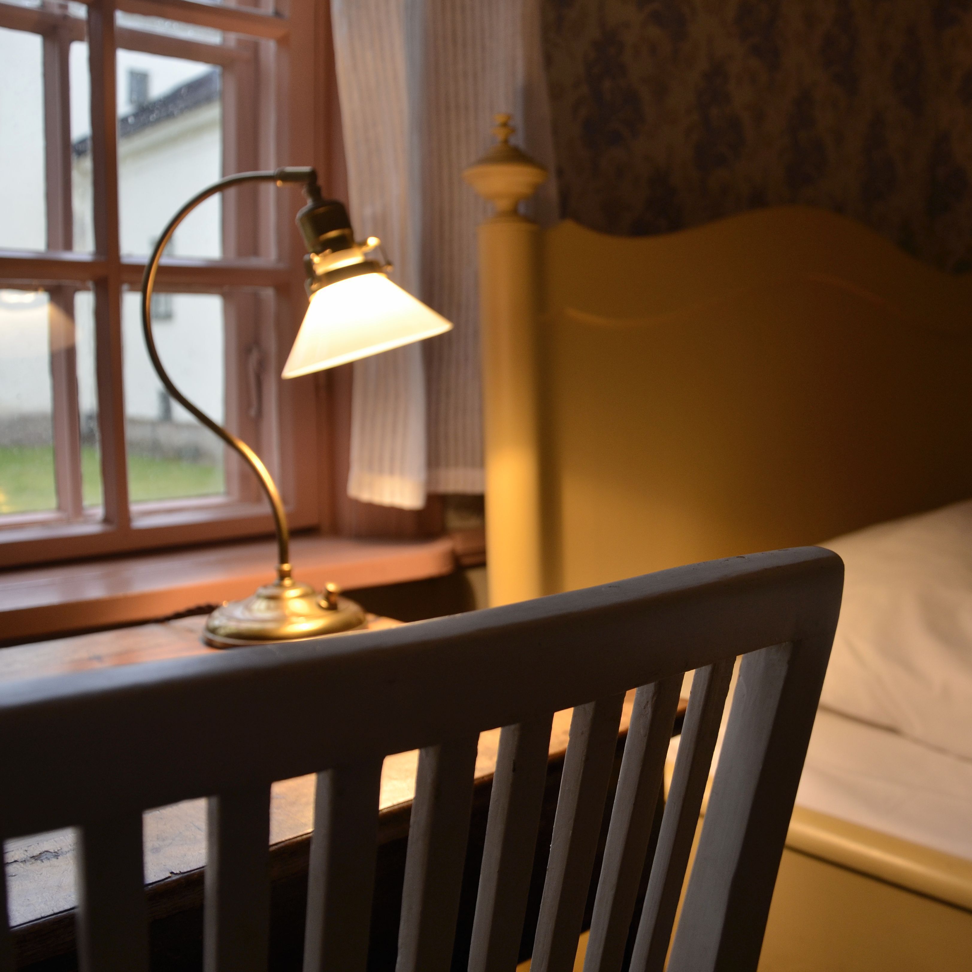 A wooden chair in a room with a bed and a window.