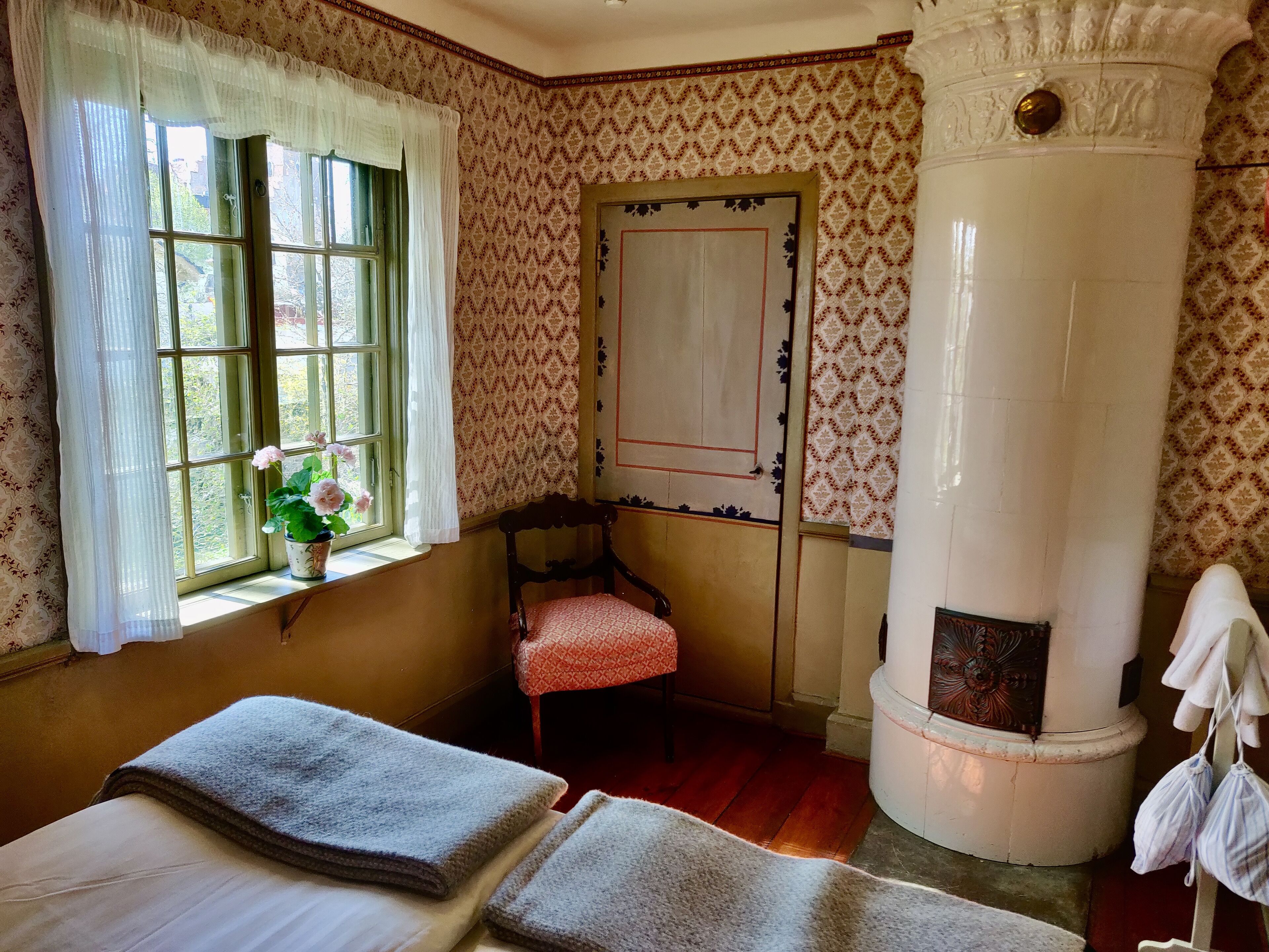 Une pièce comprenant un lit, une chaise, une fenêtre avec des rideaux, un mur à motifs et un pilier blanc.