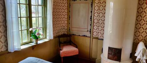 Une pièce comprenant un lit, une chaise, une fenêtre avec des rideaux, un mur à motifs et un pilier blanc.