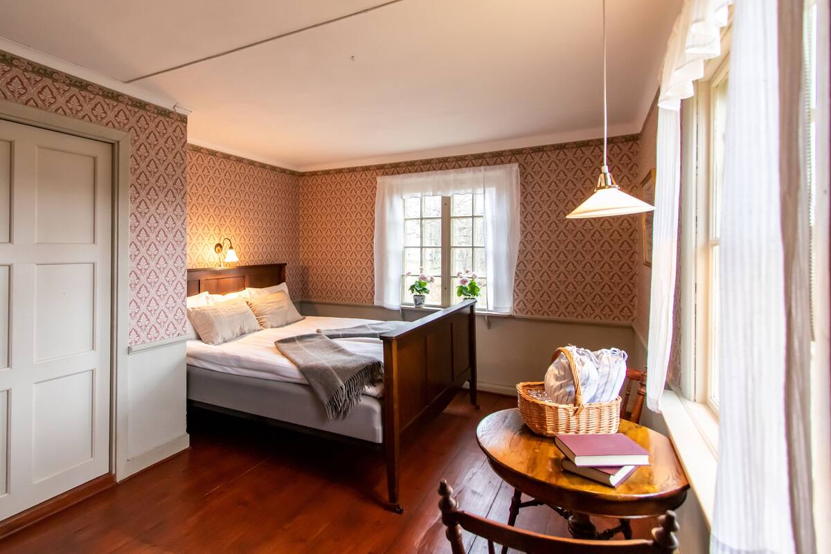 Un dormitorio con cama, mesita de noche, ventana y lámpara colgante.