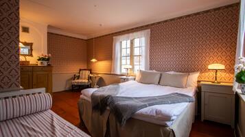 A bedroom with a large bed, a smaller bed, a chair, a desk, and a window with curtains.