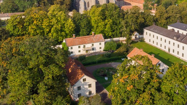 An aerial view of a historic building complex with a church, surrounded by lush greenery and a lake in the background.
