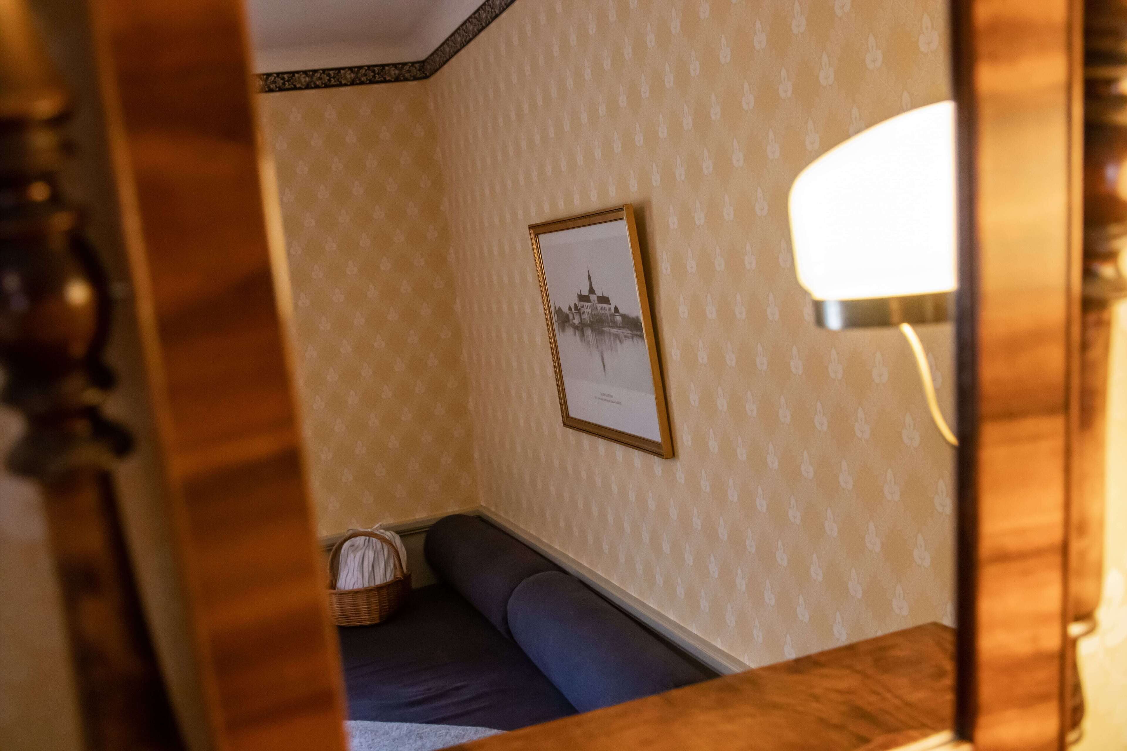 Una habitación con papel tapiz estampado, un cuadro en la pared, un banco y una lámpara.