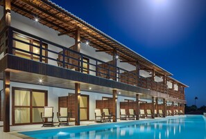 Un edificio de dos pisos con piscina, mobiliario exterior y un balcón.