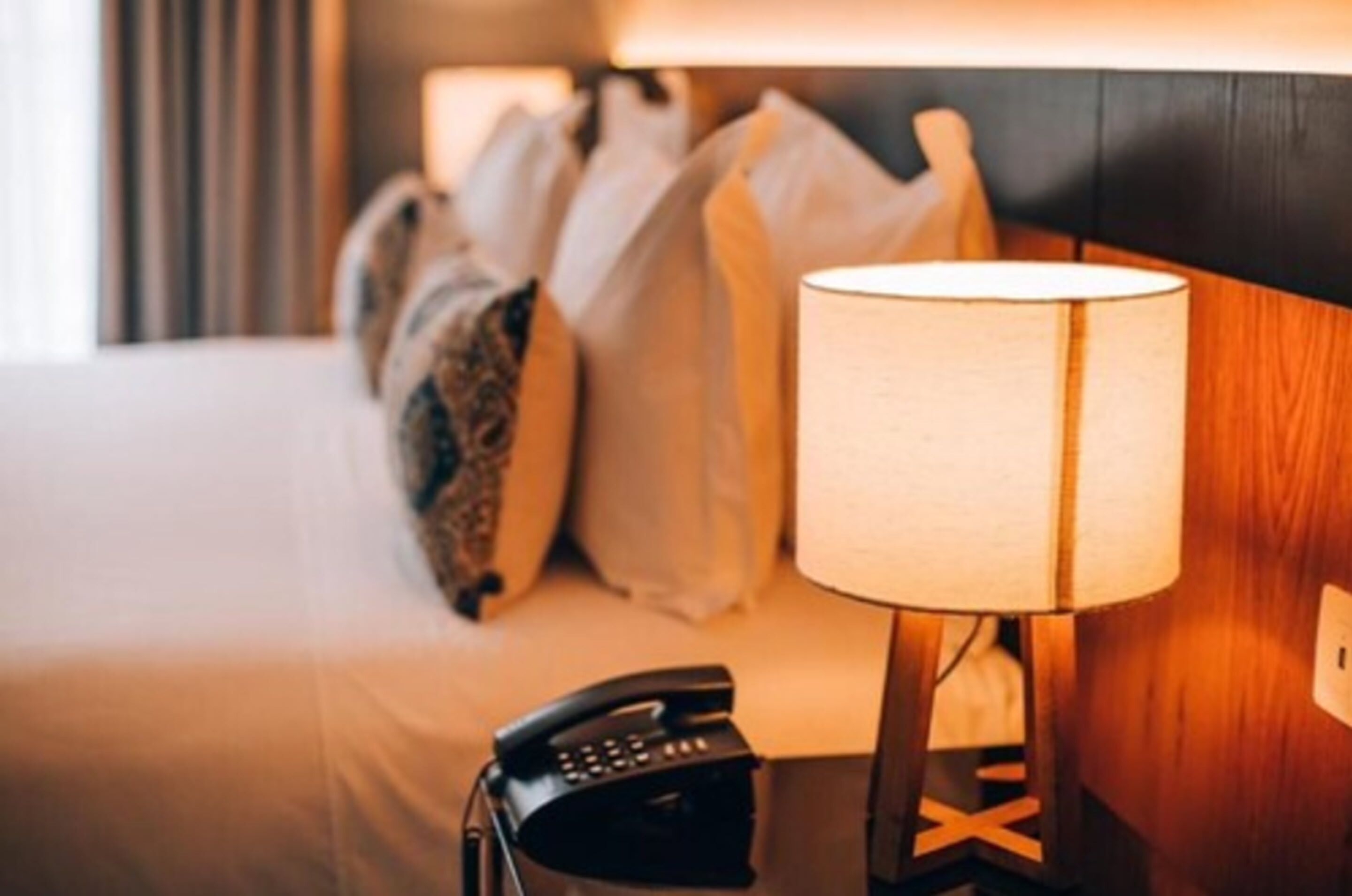 A hotel room with a bed, pillows, a bedside lamp, and a telephone.