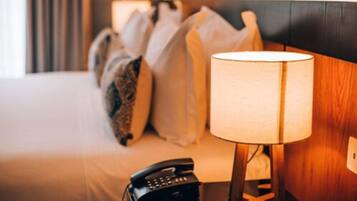 A hotel room with a bed, pillows, a bedside lamp, and a telephone.