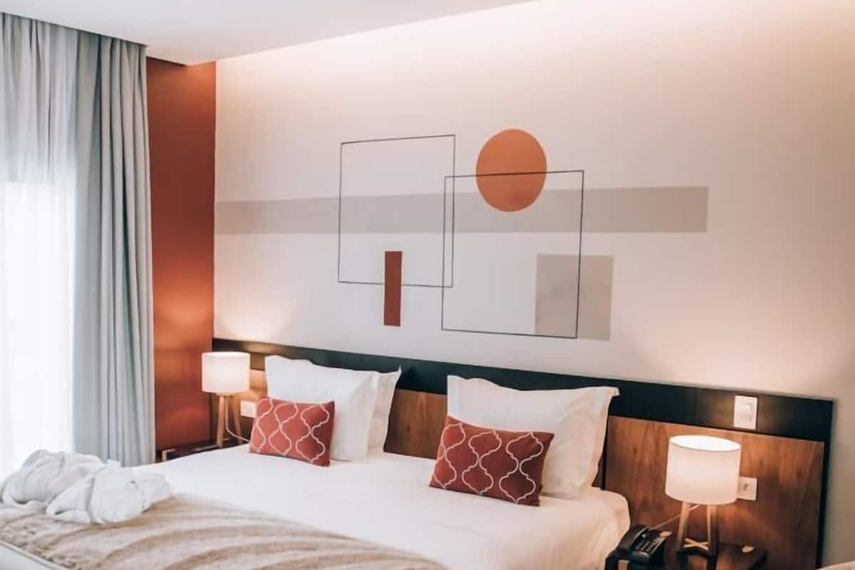 Una habitación de hotel con una cama grande, dos mesitas de noche, una silla y una obra de arte colgada en la pared.