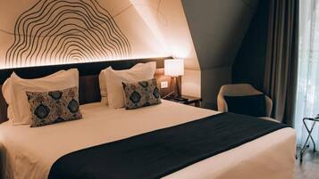 A hotel room with a large bed, a headboard with a unique design, a bedside table with a lamp, and a chair.