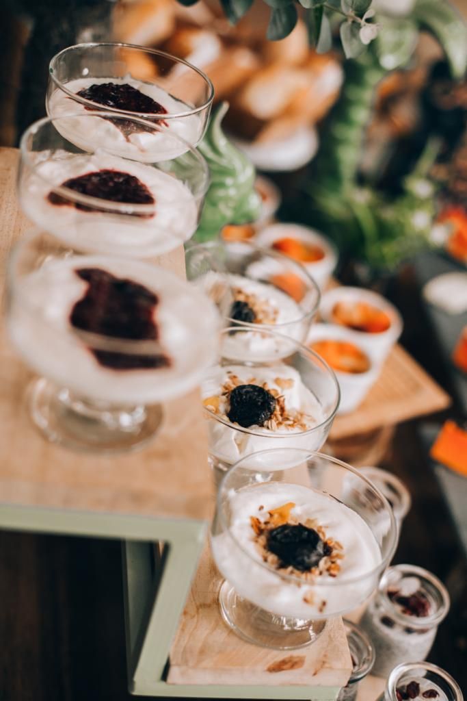 Varios vasos con postres en capas, posiblemente a base de yogur, con ingredientes como granola y frutos rojos, dispuestos sobre una tabla de madera.