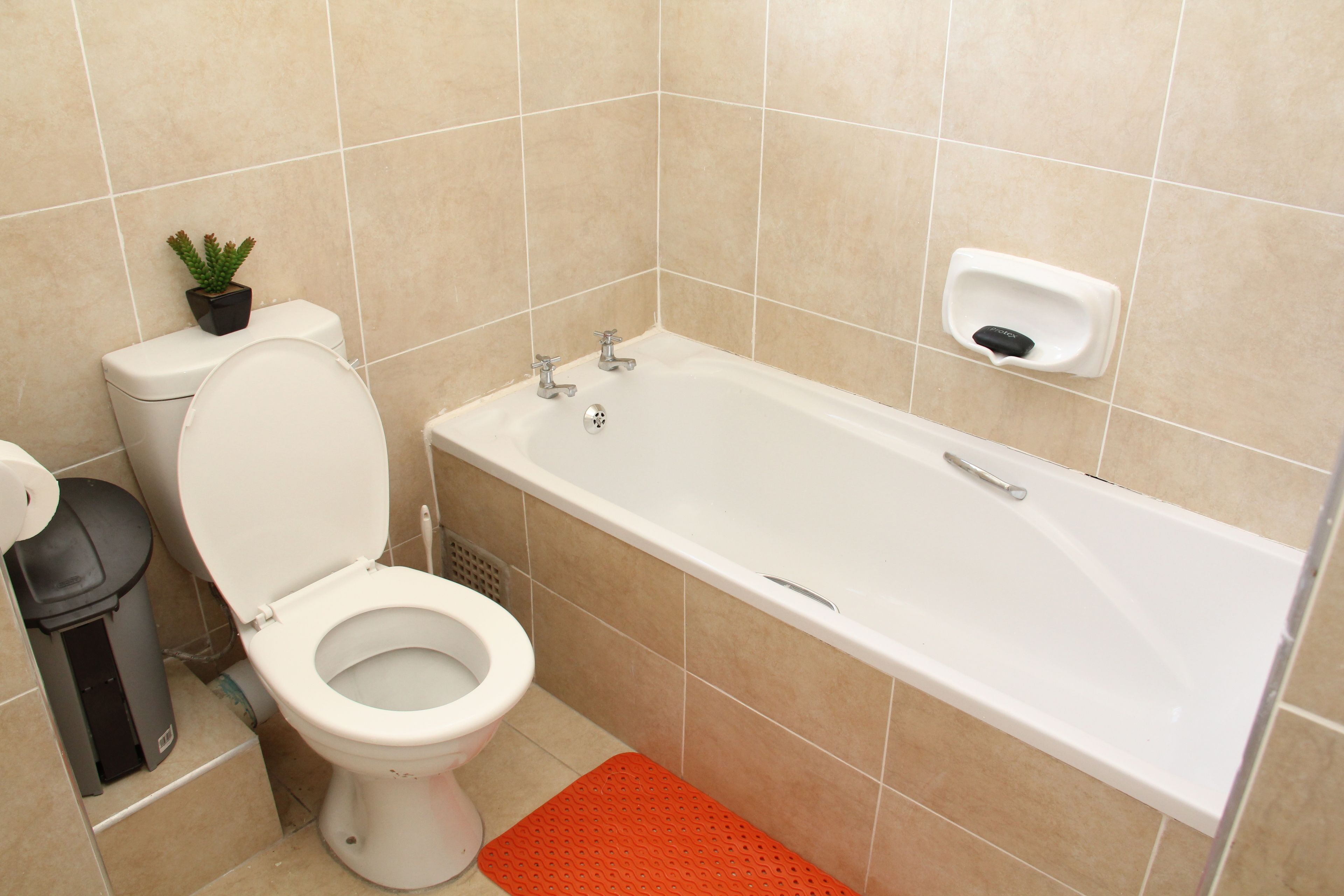 A bathroom with a toilet, a bathtub, and a hand soap dispenser.