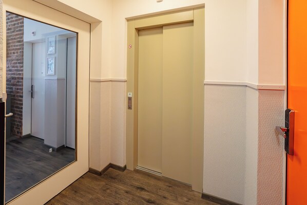 A hallway with a wooden floor, a glass door, an elevator, and a brick wall. - easyHotel Zürich City Limmatplatz (Zürich)