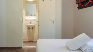 Une chambre d’hôtel comprenant un lit, une salle de bain avec un lavabo et un miroir, et un porte-serviettes fixé au mur.