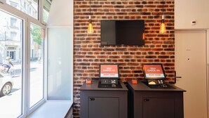 A self-check-in kiosk with a brick wall backdrop and a mounted TV. - easyHotel Zürich City Limmatplatz (Zürich)