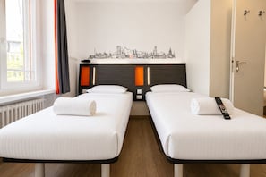 Ein Hotelzimmer mit zwei Einzelbetten, einem Stadtbild an der Wand, einem Fenster mit Vorhängen und einer Tür.