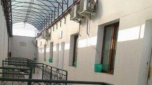 A covered outdoor area with a metal railing, air conditioning units, and a window with a green bucket. - Hotel Khiva (Tashkent)