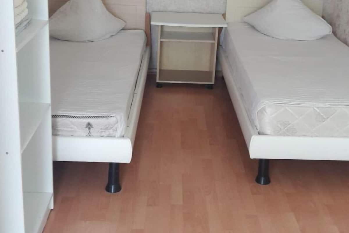 Une petite chambre à coucher, bien rangée, avec deux lits, une armoire blanche et une petite table.