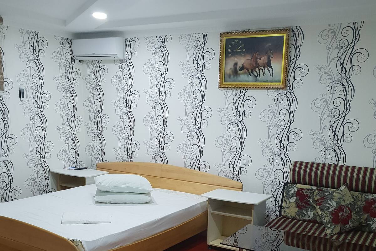 Une chambre à coucher avec un lit en bois, un tapis rouge à motifs, un canapé et un mur orné d’un motif décoratif.