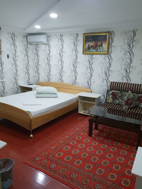 A bedroom with a wooden bed, a red patterned rug, a sofa, and a wall with a decorative pattern.