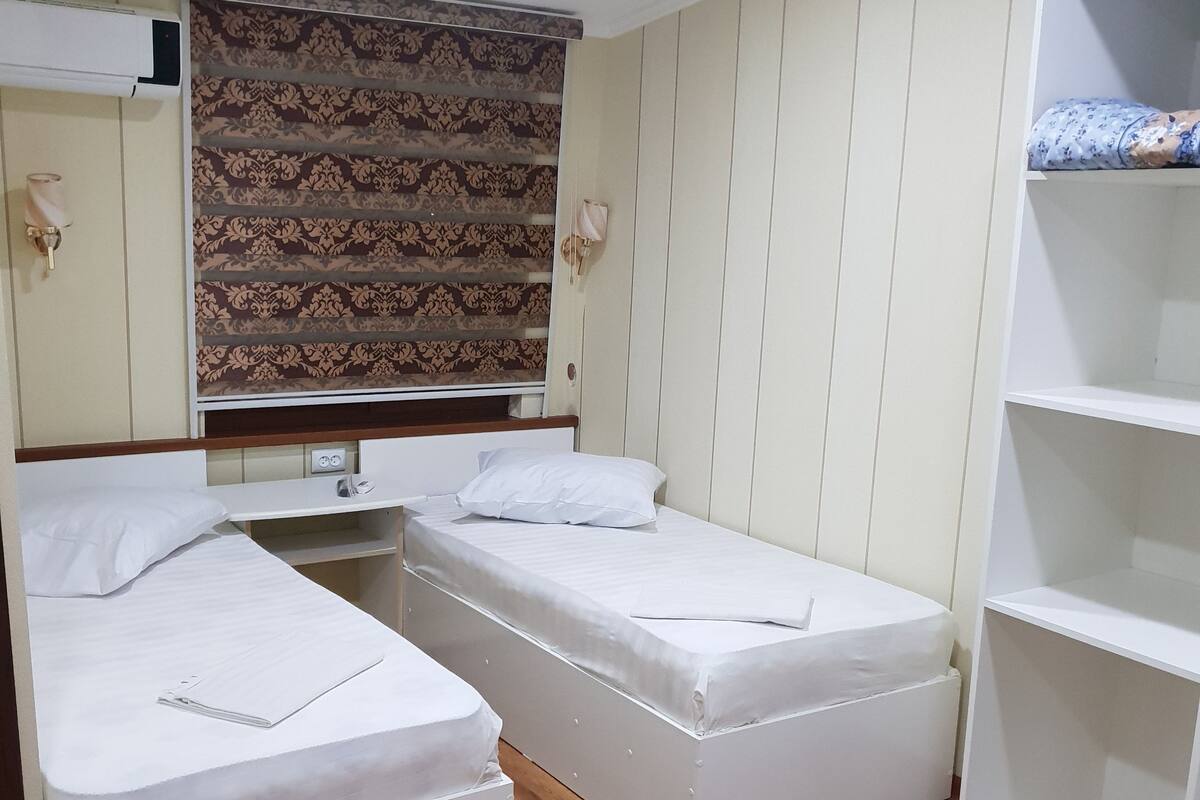 Une petite chambre compacte, équipée de deux lits simples, d’une armoire et d’une étagère.