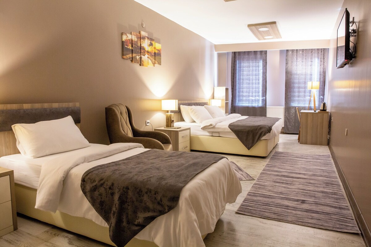 A hotel room with two beds, a desk, a chair, a TV, and a window with curtains.