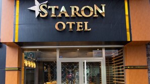 Das Hotel Staron mit auffälliger Beschilderung, großen Glasüren und einem gelben Sitzbereich, der durch den Eingang sichtbar ist.