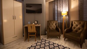 Ein Hotelzimmer mit Schreibtisch, zwei Sesseln, Fernseher und Lampe.