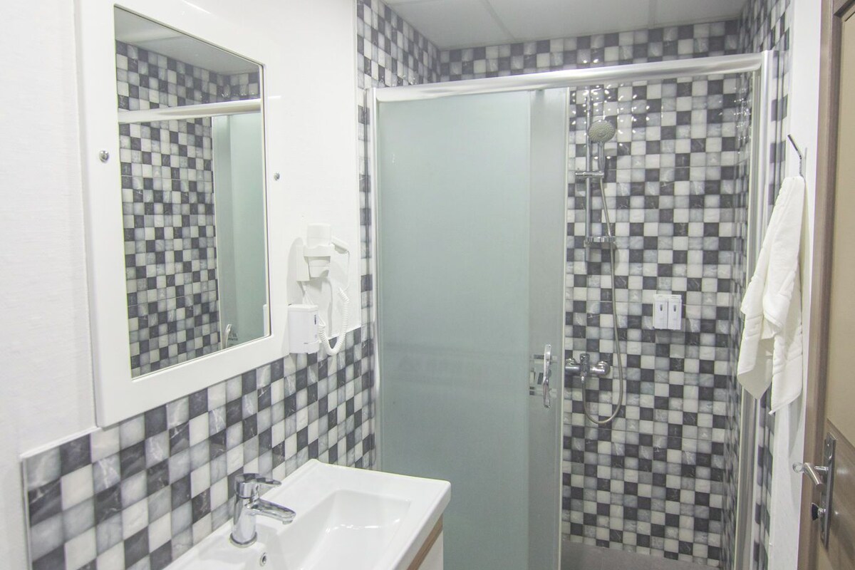 A bathroom with a checkered tile wall, a glass shower enclosure, a white sink, and a mirror.