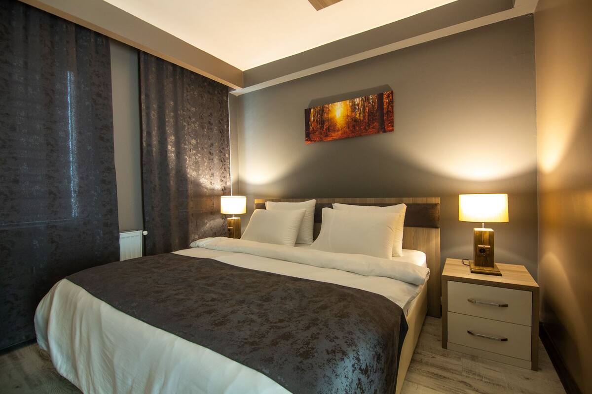 Une chambre d’hôtel moderne avec un grand lit, deux tables de chevet avec des lampes, une commode et un tableau au mur.
