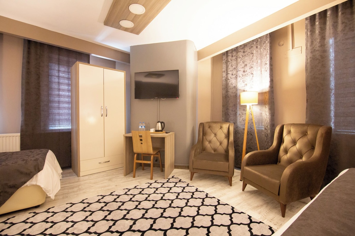 A hotel room with a bed, a desk with a chair, a television, a lamp, and a large window with curtains.