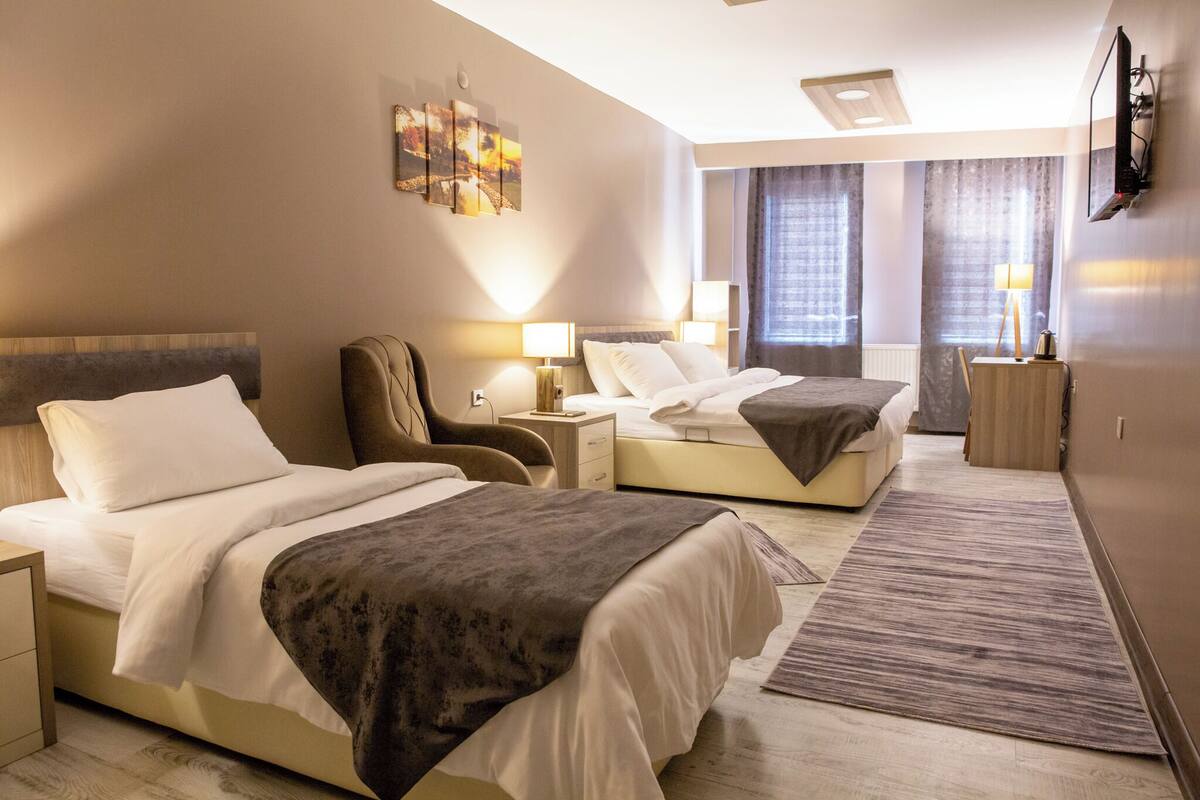 Une chambre d’hôtel avec deux lits, un bureau, une chaise, une télévision et une fenêtre avec des rideaux.