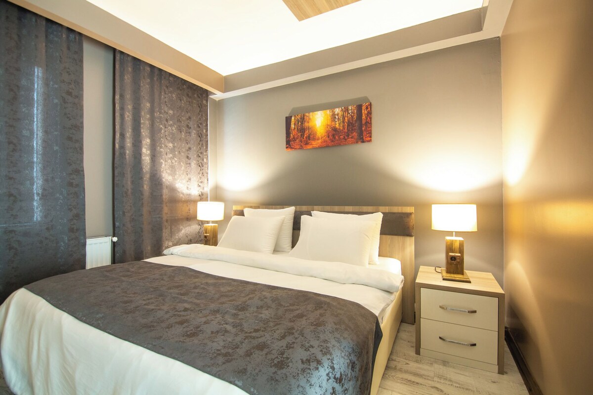 A hotel room with a large bed, two bedside tables with lamps, a painting on the wall, and a window with curtains.