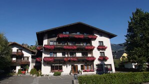 Un hôtel à plusieurs étages, doté de balcons ornés de fleurs, d’un parking et surplombant un paysage montagneux.