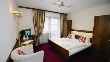 Ein Hotelzimmer mit Doppelbett, Schreibtisch mit Lampe, Sessel, Fernseher und großem Kleiderschrank.