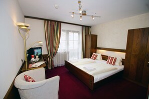 A hotel room with a double bed, a desk with a lamp, a chair, a television, and a large wardrobe. - Pension Heidi (Kaprun)