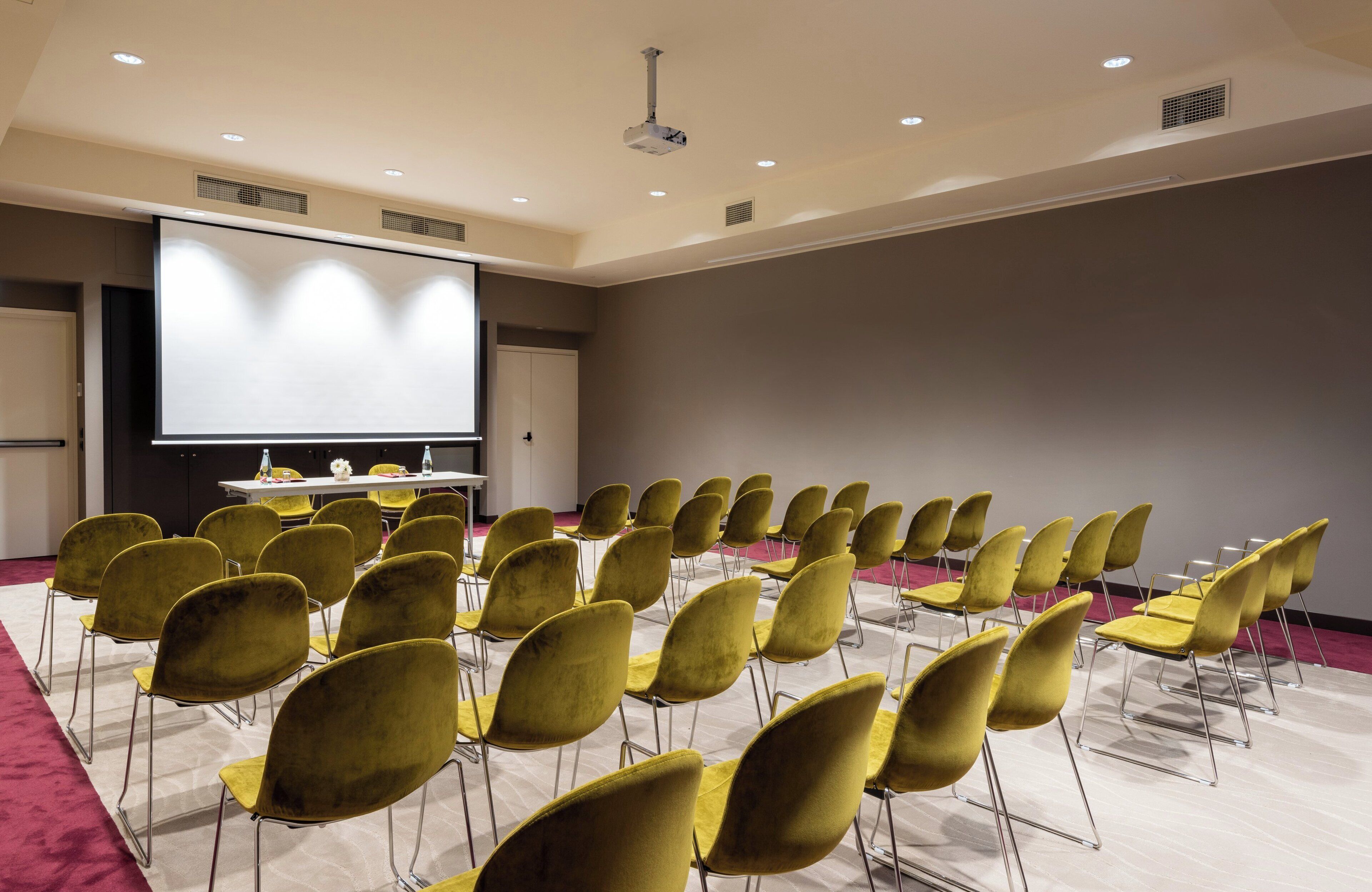 A conference room with rows of yellow chairs, a large screen, and a podium.
