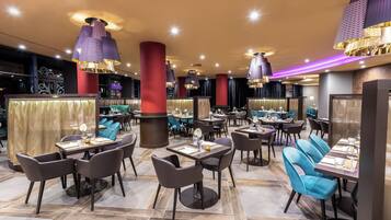 Ein modernes Restaurant mit mehreren Esstischen, Stühlen und dekorativer Beleuchtung.